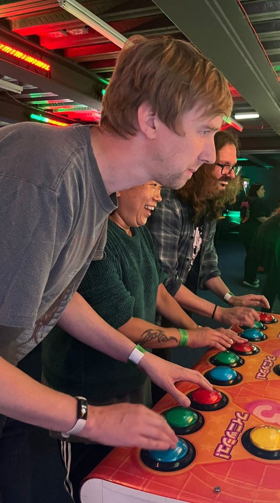 picture of three devs on an arcade machine, two men and a woman in the centre laughing